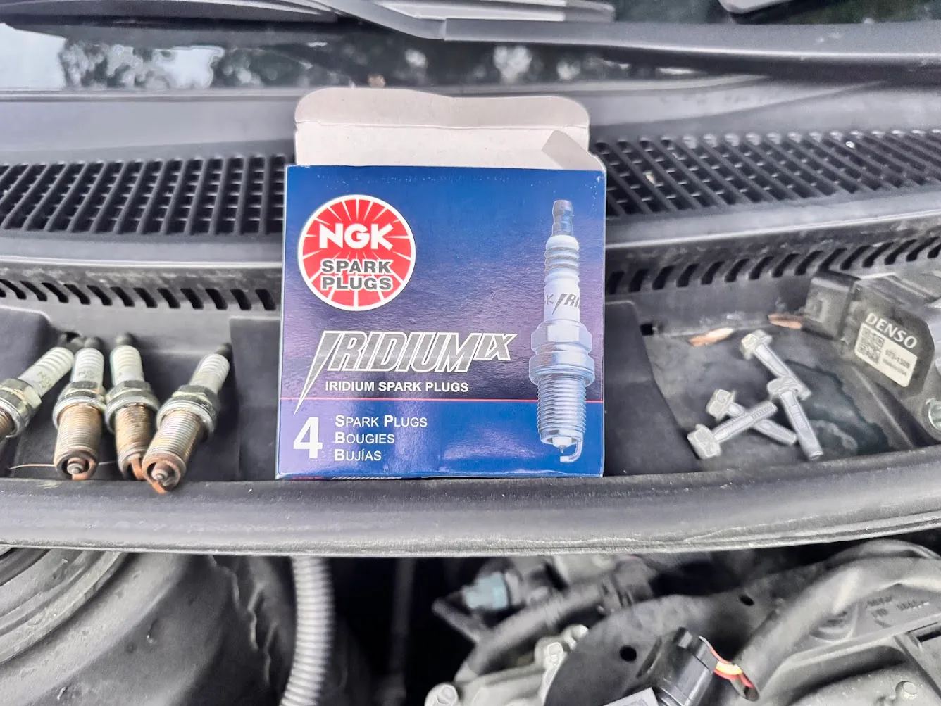 New NGK Iridium IX spark plugs beside the removed old plugs