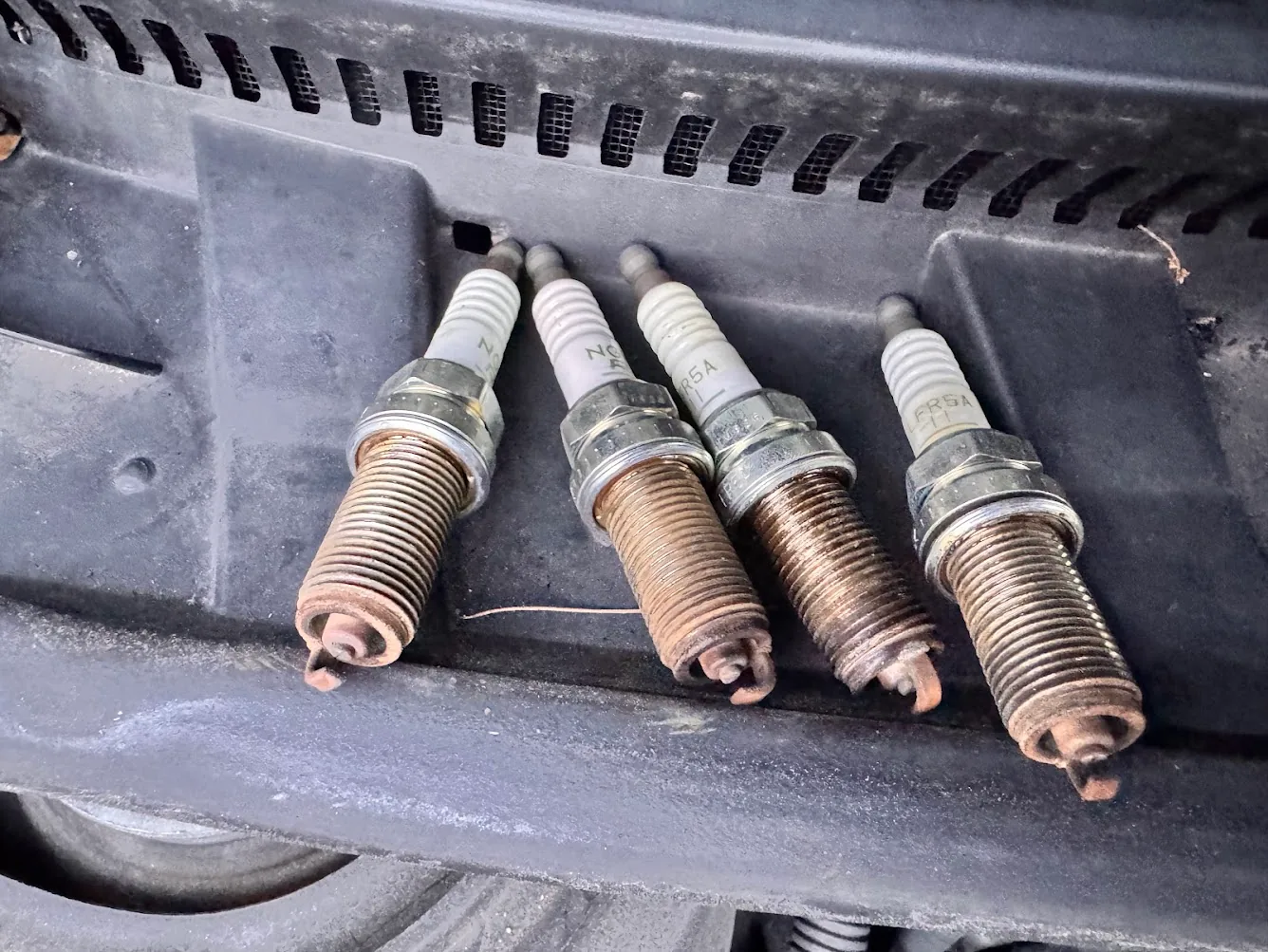 Four old spark plugs removed from a 2012 Scion tC